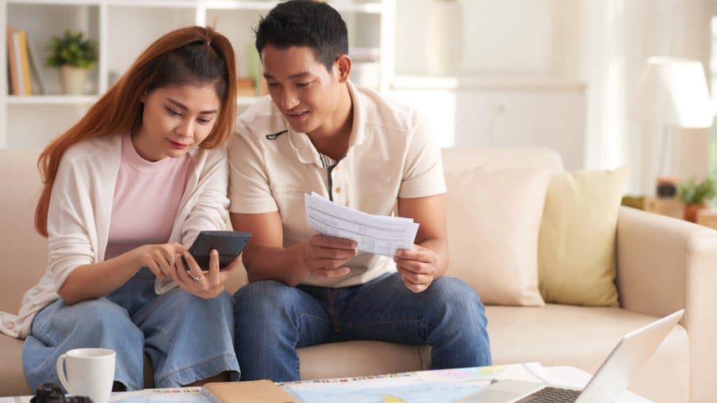 Couple calculating finances using a calculator and papers over a map.