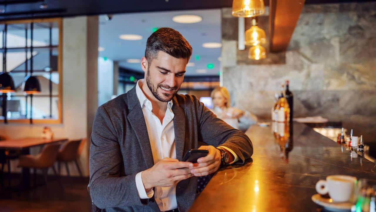A man at a bar smiles while looking at his phone.