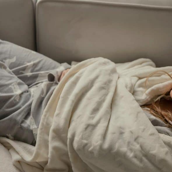A woman lying on a couch wrapped in a blanket.