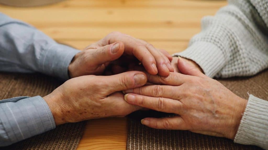 An elderly couple gently holding hands across a table.