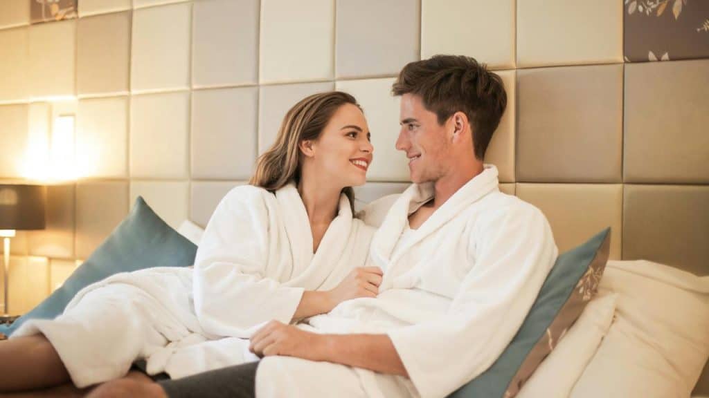 A couple in white robes relaxing together on a bed.