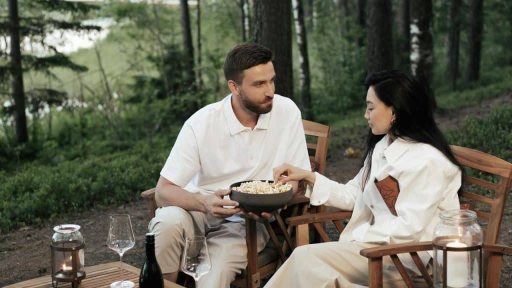 A couple sitting outdoors sharing a bowl of popcorn.