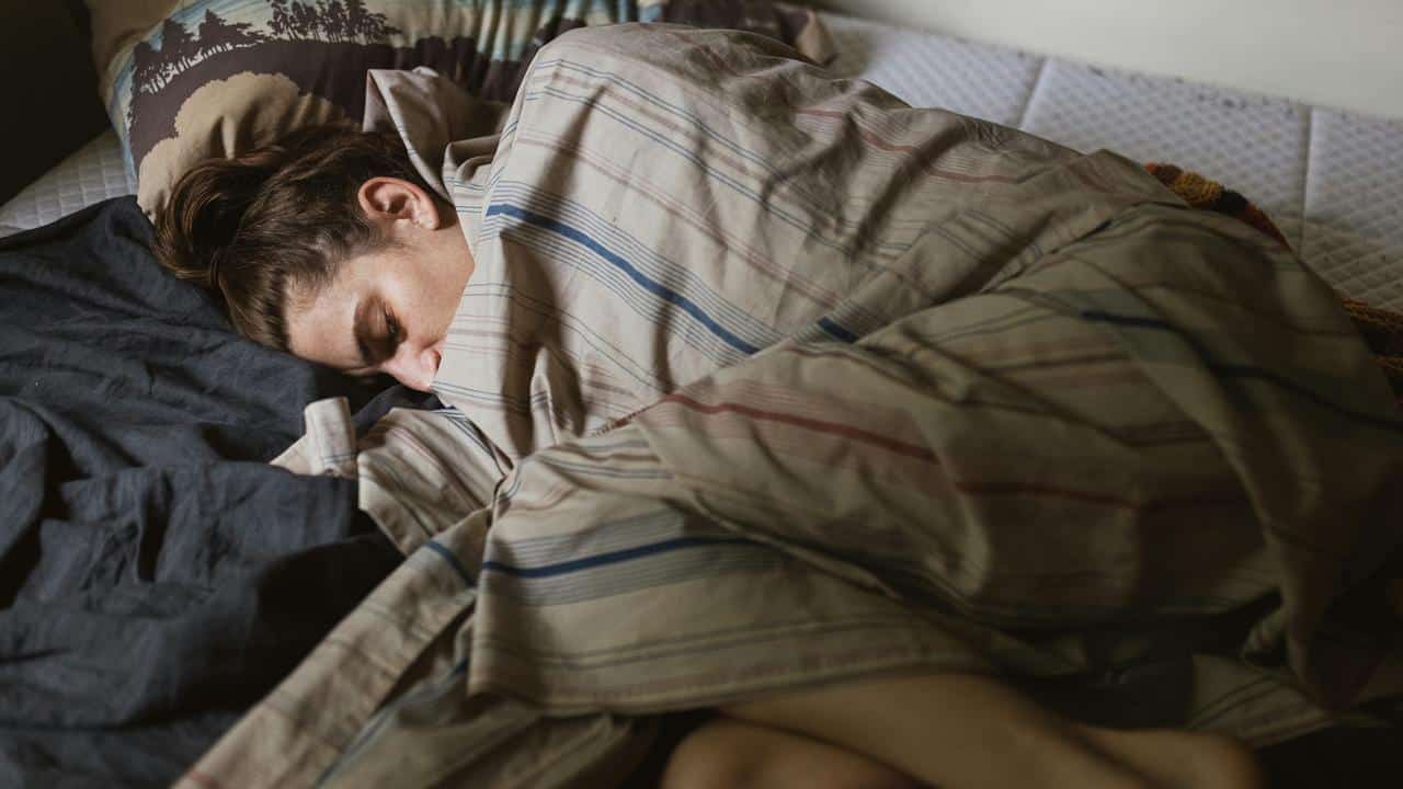 A person sleeping in bed wrapped in a striped blanket.