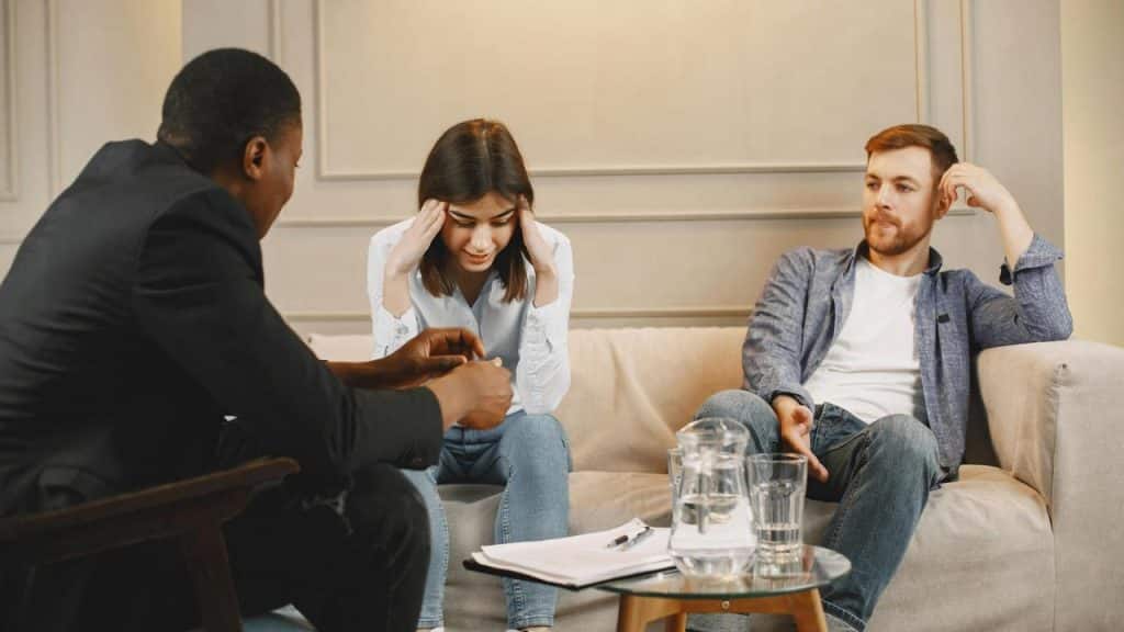 A distressed woman sitting between two men during a counseling session.