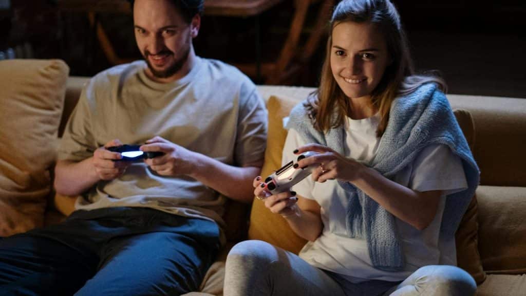 A man and woman smiling while playing video games on a couch.