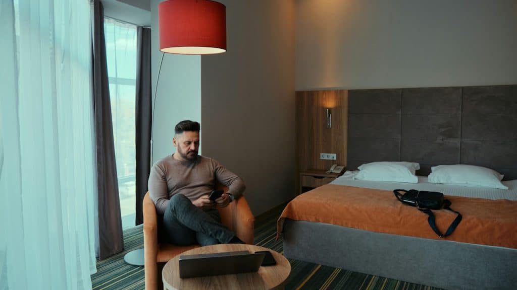 A man is sitting in an armchair in a room, looking at his phone.