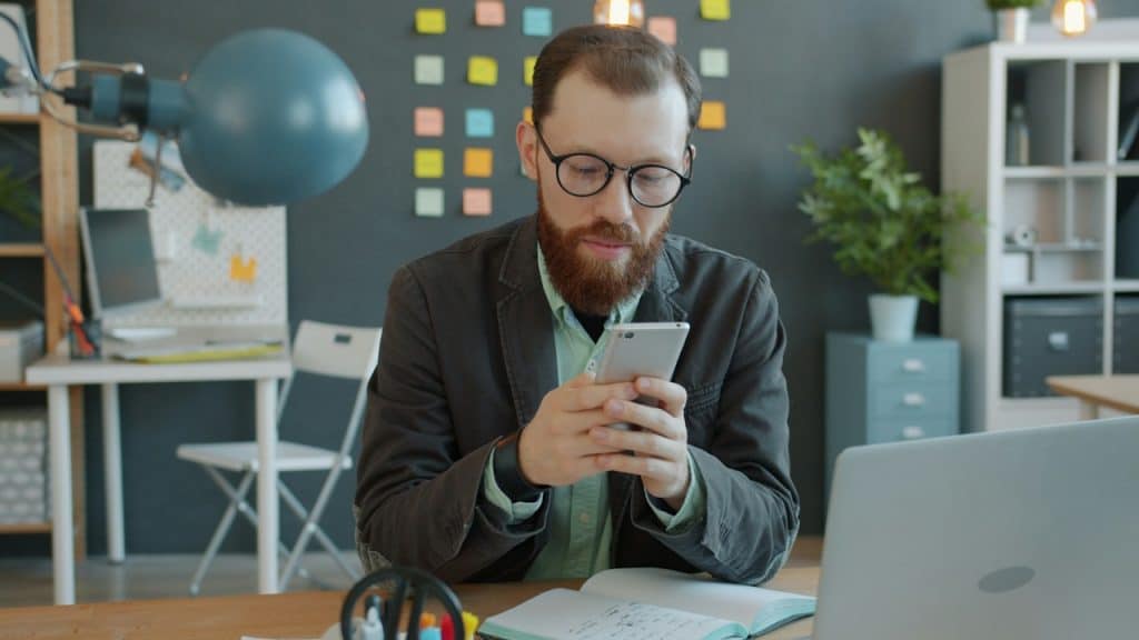 A man texting on his phone while sitting in his office.