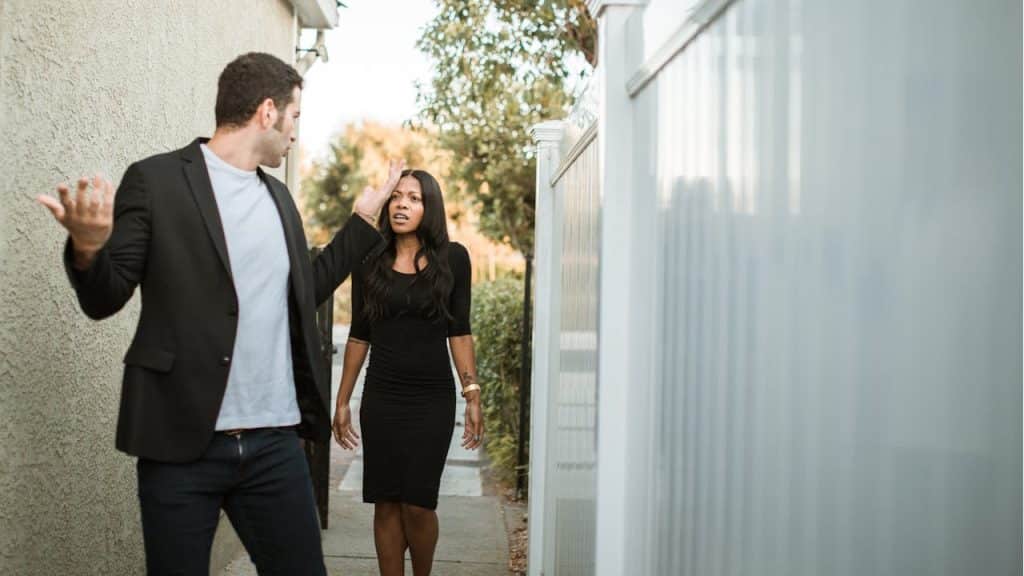 A man in a suit jacket is arguing with a woman in a black dress while standing on a narrow walkway.