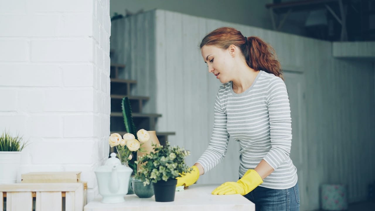 A woman wearing yellow gloves is cleaning a table.