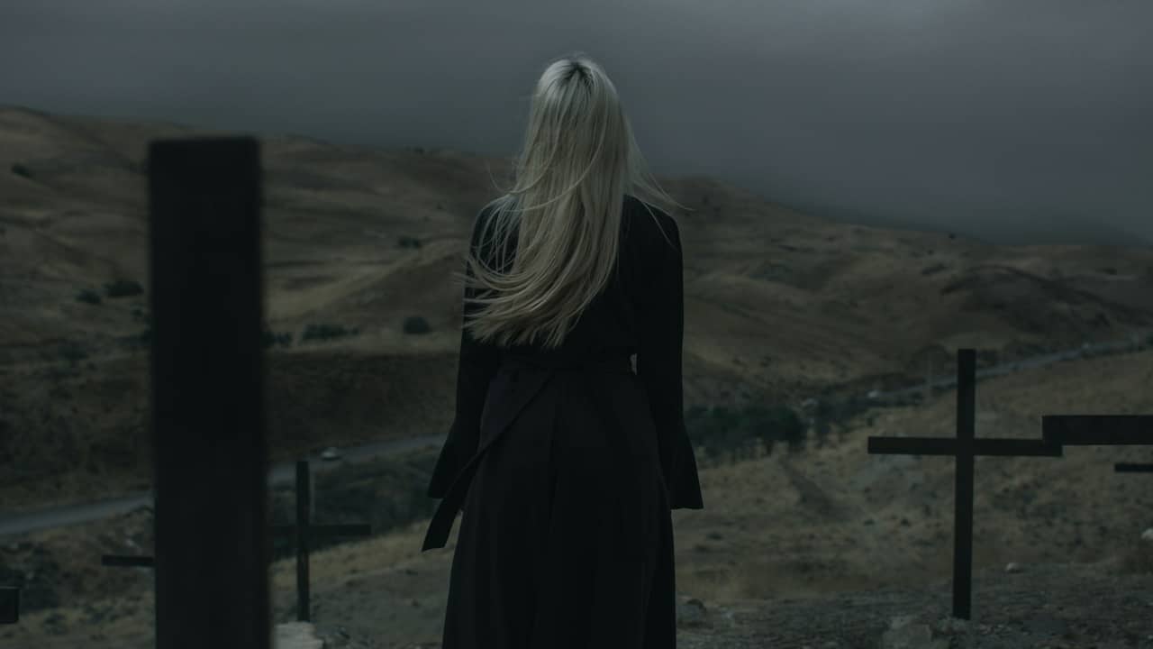 A woman standing amongst graves on a hill in the evening.