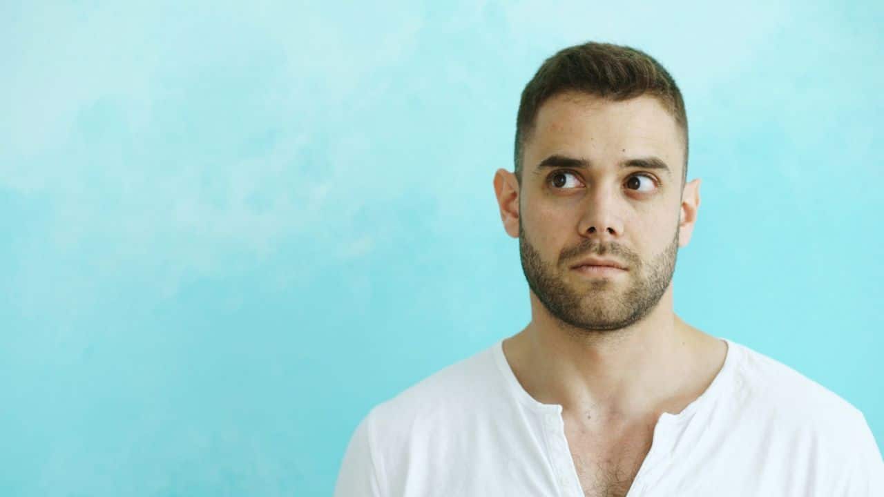 A man with a beard and short hair looks away against a blue background.