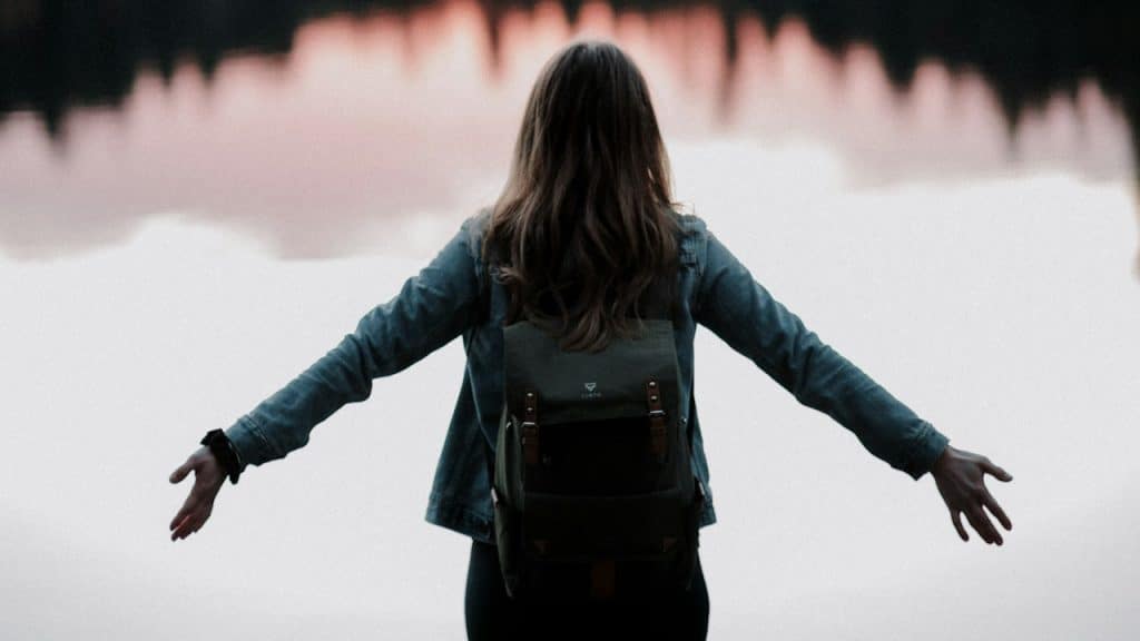 A woman standing while facing on body of water.