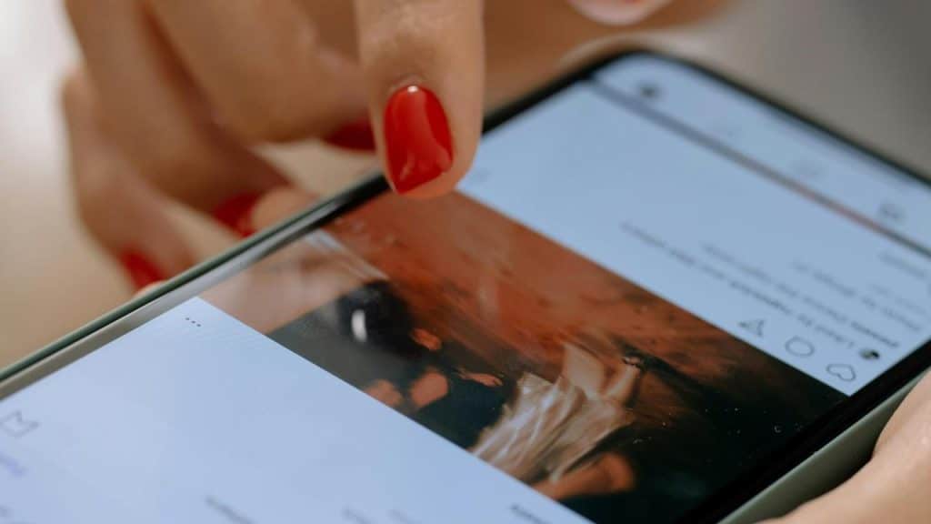 A close-up of a hand with red nail polish scrolling on a smartphone screen.