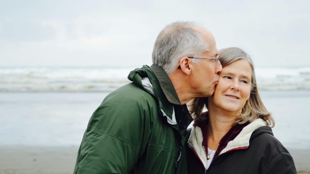 A man kissing a woman while they stand on a beach.