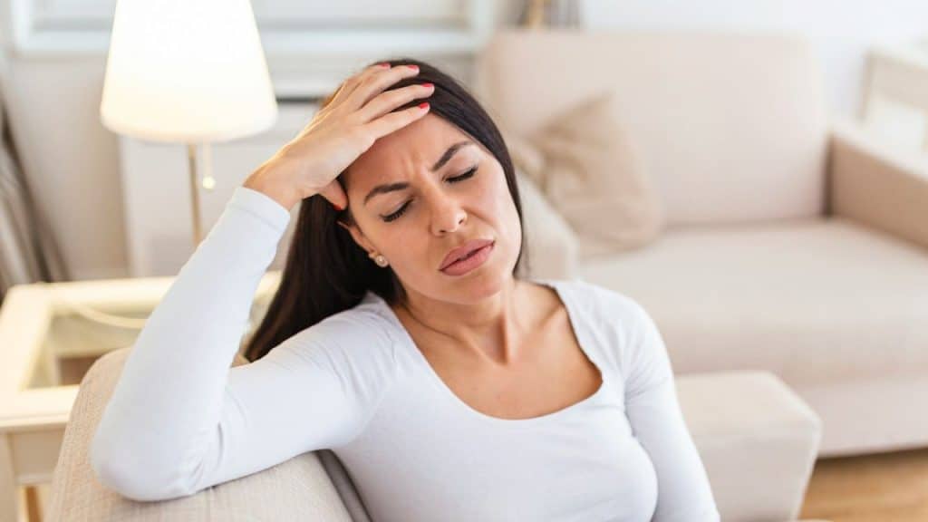 Frustrated woman with hand on forehead sitting on a couch indoors.