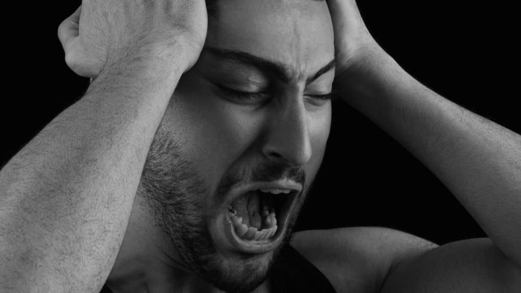 Black and white close-up of a man yelling with hands on his head.