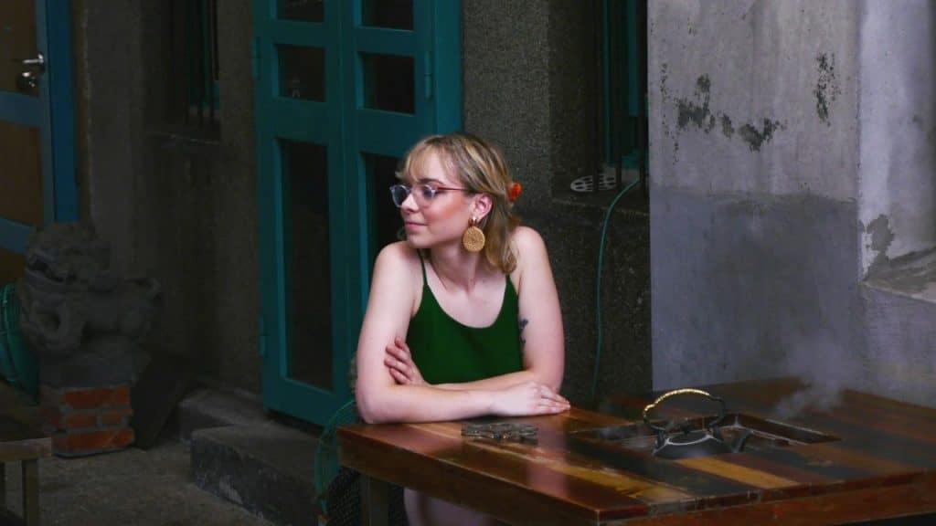 Blonde woman in glasses and a green top sitting at an outdoor wooden table.