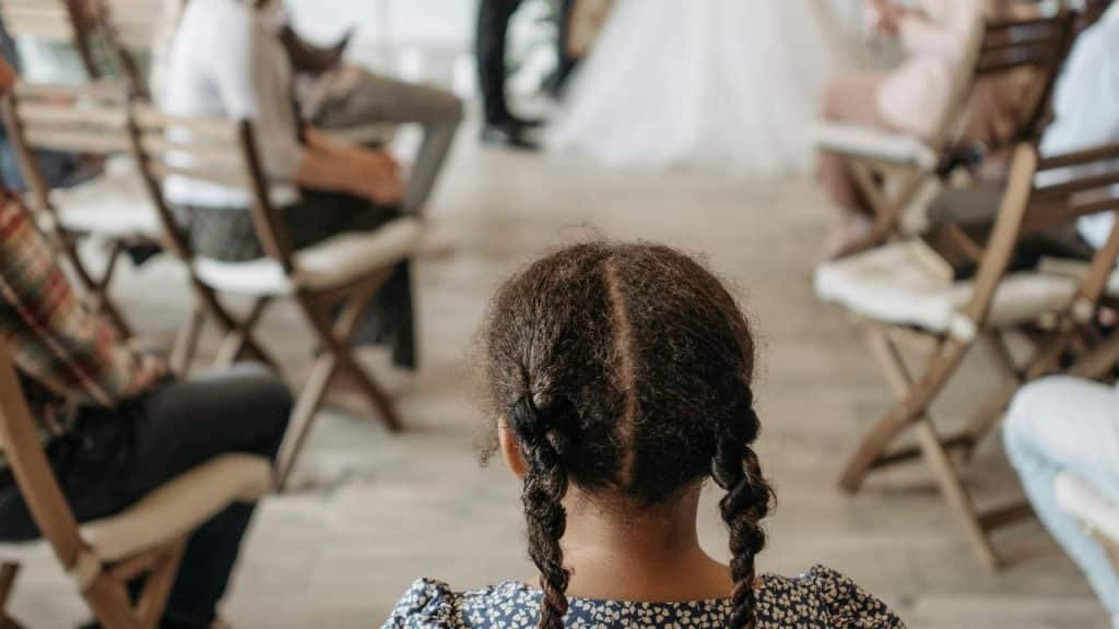 A young girl with braided hair watches a wedding ceremony.