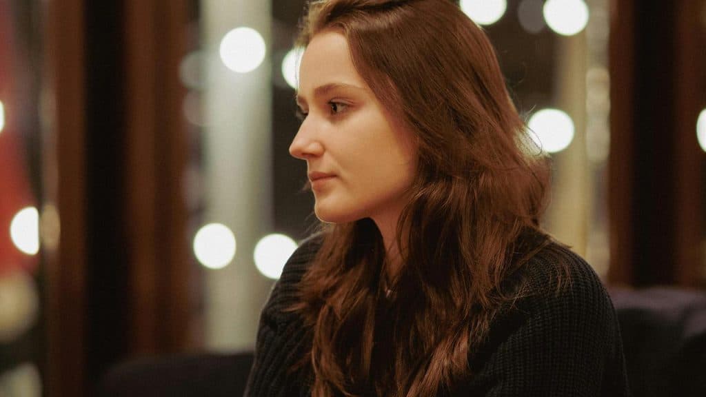 A woman with brown hair sitting indoors, looking to the side.