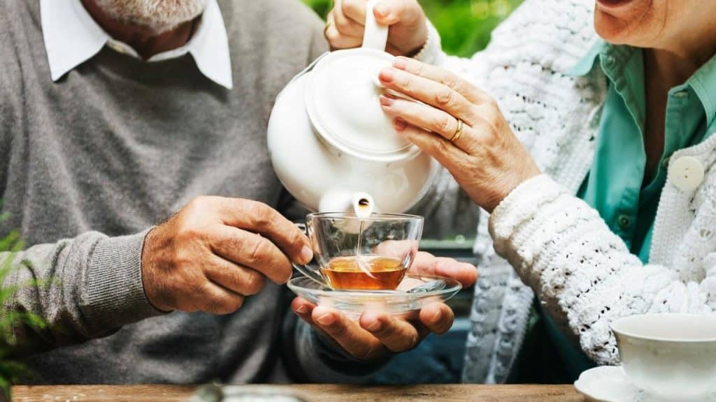 A person pours tea into another’s cup at an outdoor table.