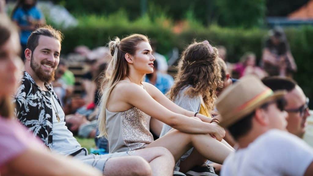 People sitting outside in a crowd; a woman in a sparkly top smiles while a man grins.