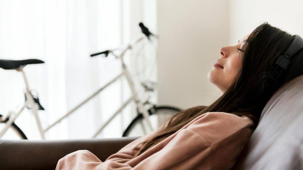 A woman relaxing on a couch while listening to music with headphones.