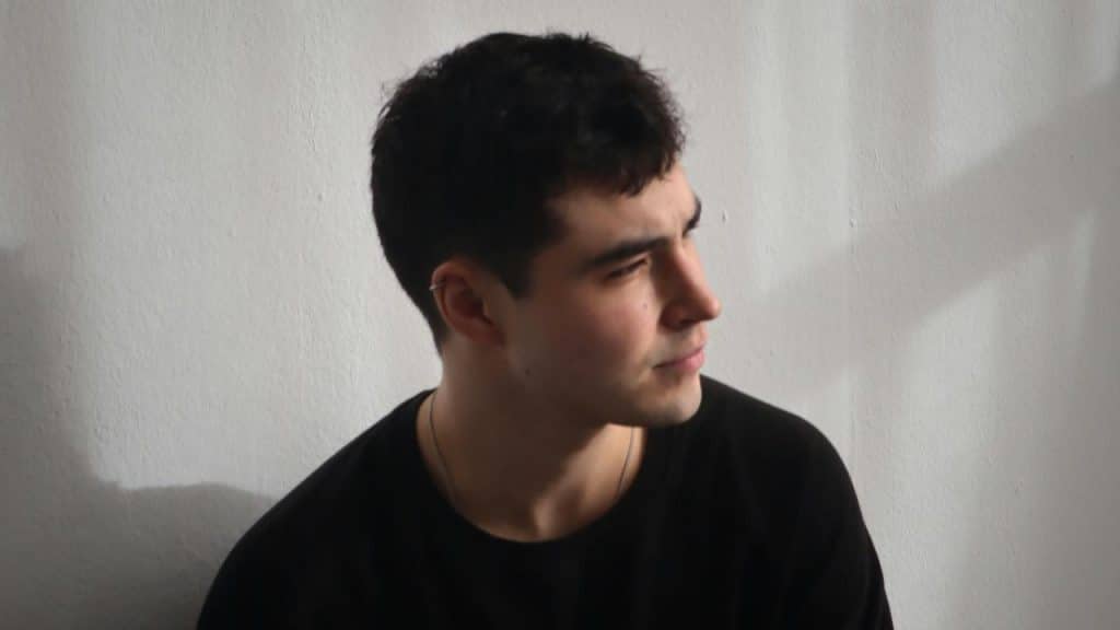 A man in a black shirt looking to the side in soft, natural light.