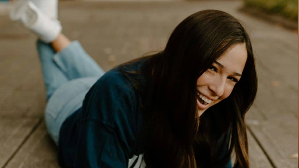 A woman in a blue t-shirt and blue denim jeans sitting on a concrete floor during daytime.