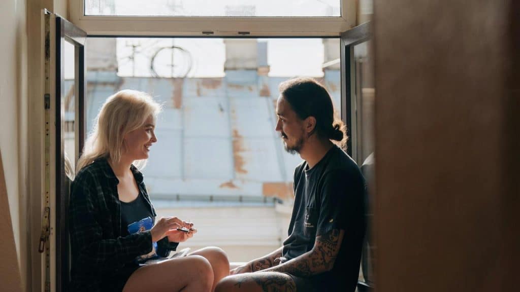 A couple sitting by an open window, talking and smiling.