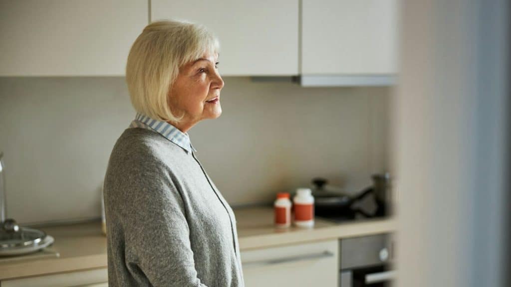 Older woman with short blonde hair standing in a kitchen, looking to the side.