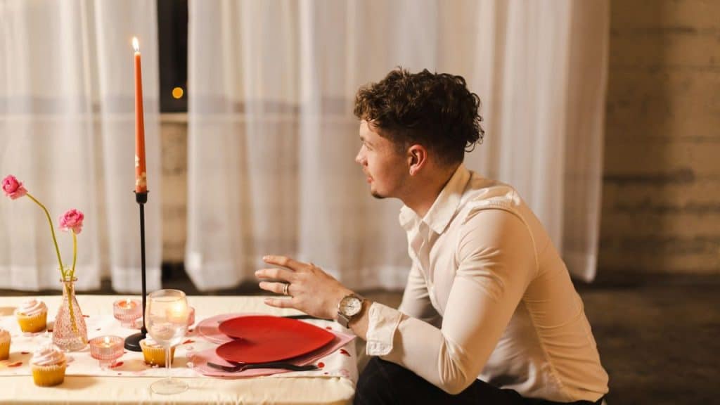 Young man sitting at a table set for a romantic dinner with a candle and heart.