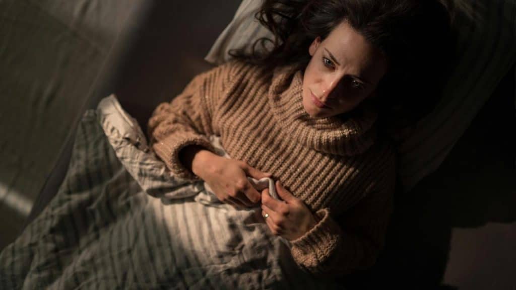 A woman lying in bed wearing a brown sweater.