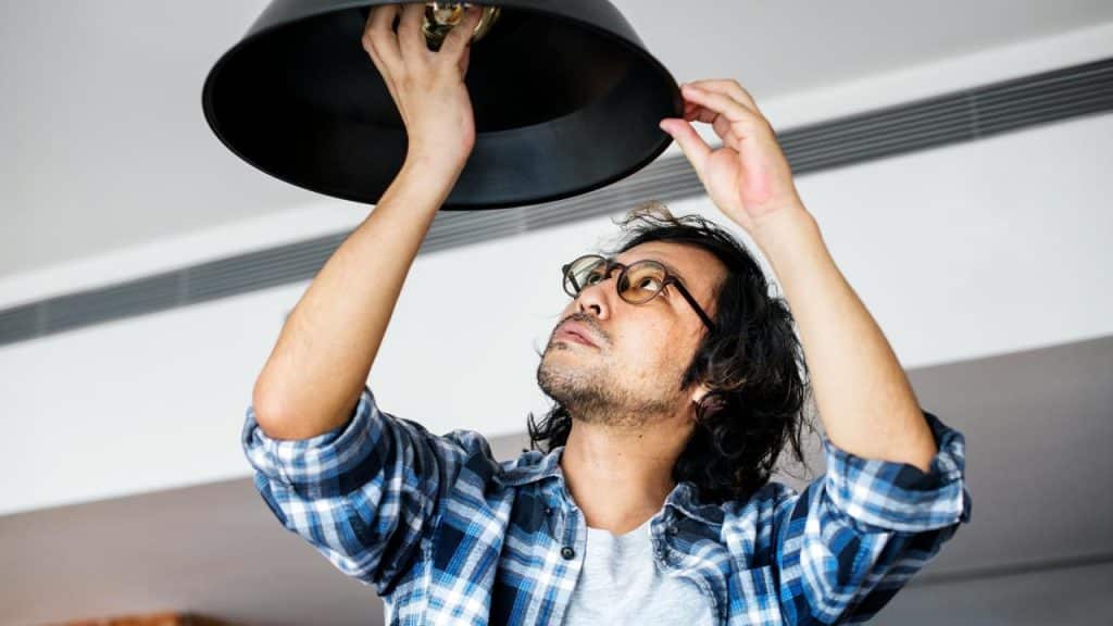 A man wearing glasses and a plaid shirt fixing a ceiling light.