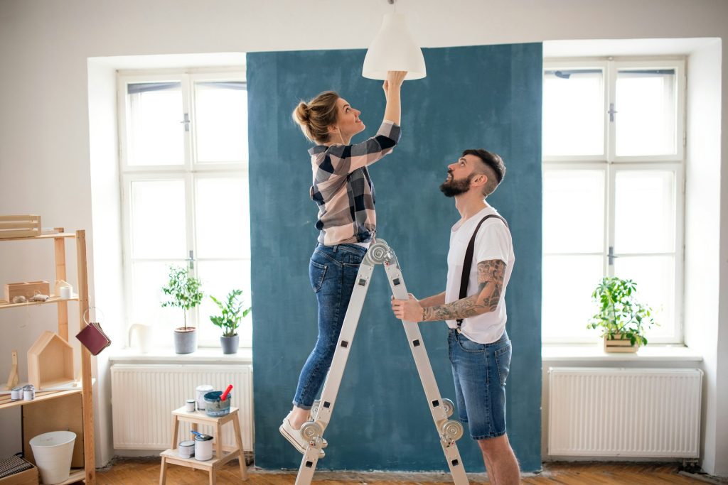 A woman changing a lightbulb while a man holds the ladder.