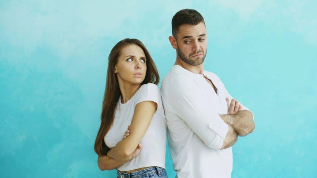 A man and woman standing back-to-back with crossed arms against a blue wall.