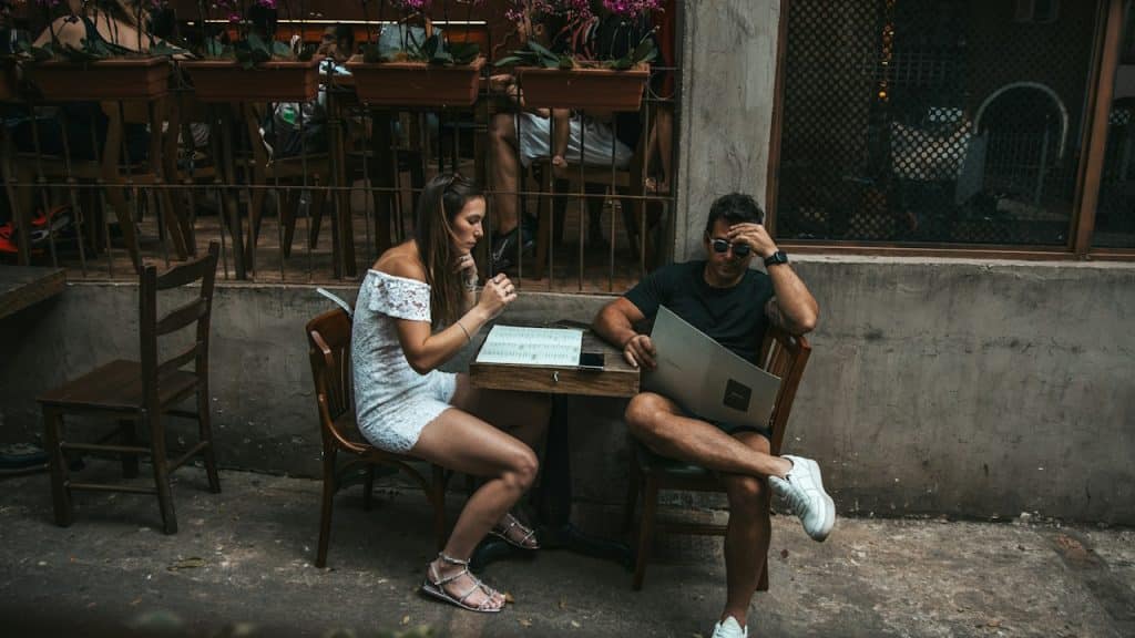 A man is reading a menu card while her wife is sitting silently at the table.