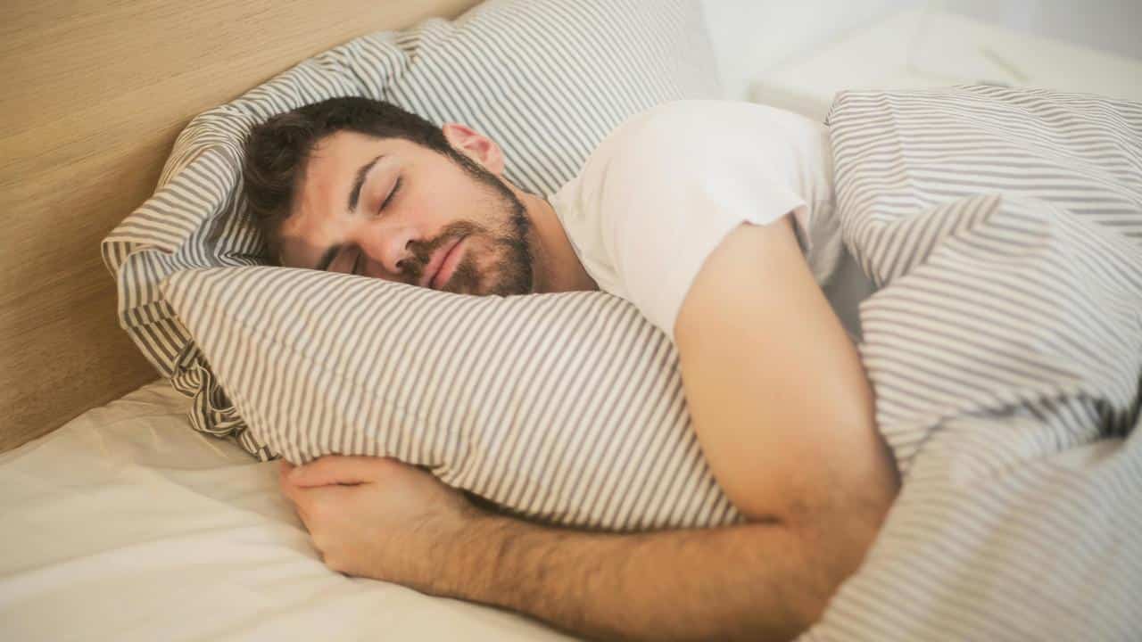 A man with a white shirt soundly asleep in bed.