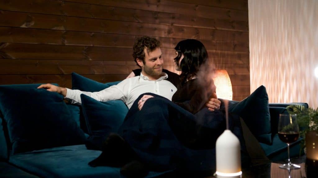 Couple embracing on a blue couch, looking at each other, in a warmly lit room.