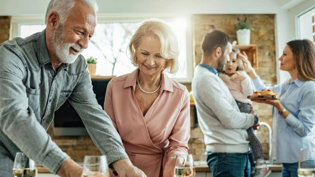 Three generations of a family smiling and interacting in a bright kitchen.