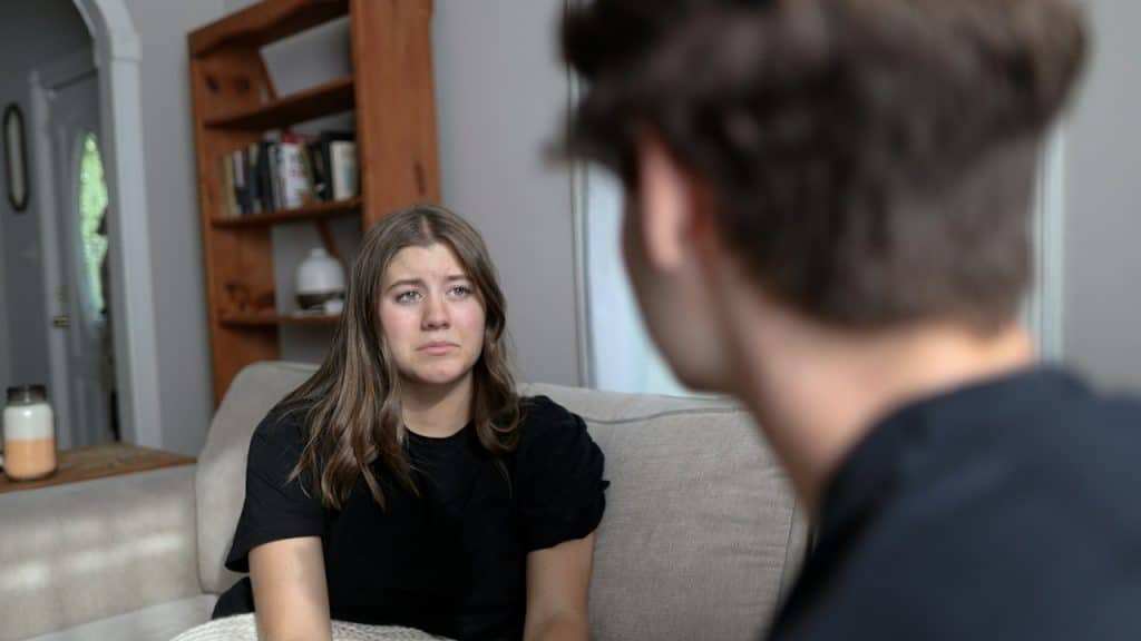 A woman looking upset and staring at a man while they sit on a couch.