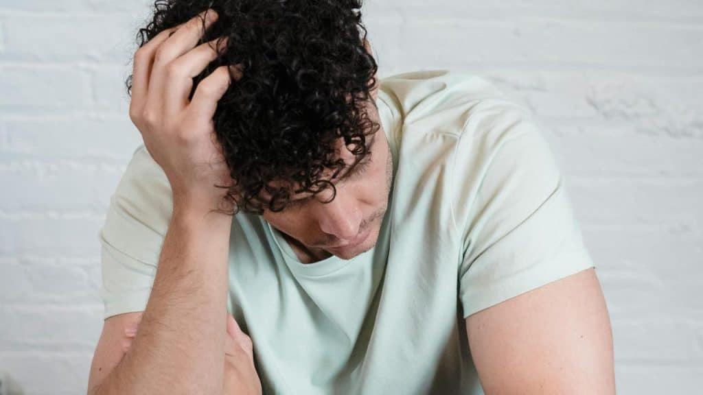 A man sitting with his head down and hand on his hair looking upset.