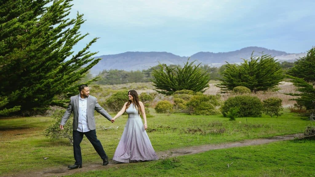 A man leading a woman through a field while holding her hand.