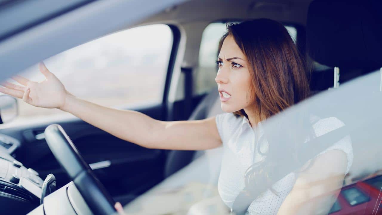 A woman in a car gesturing angrily while driving.