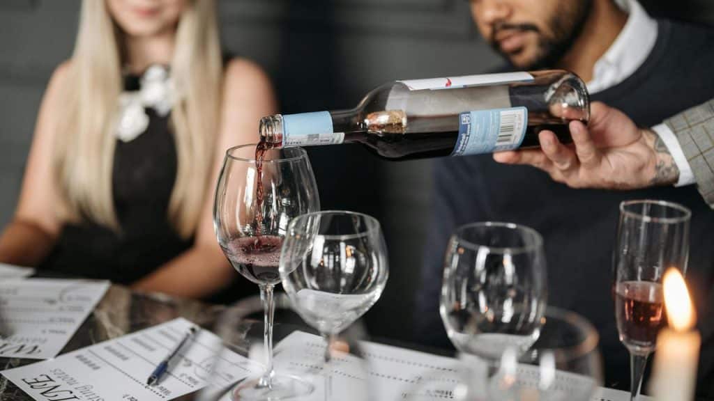 A person pouring red wine into a glass at a table with others.