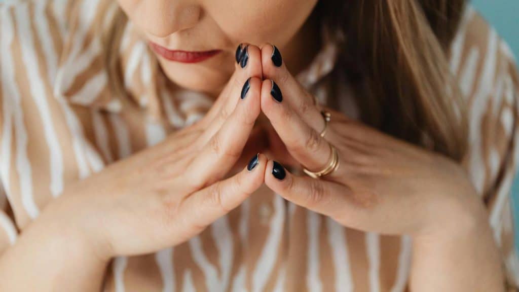A woman resting her chin on her hands with dark polished nails.