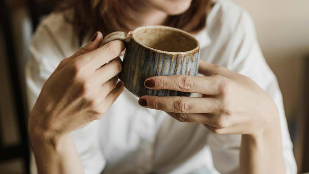 A close-up of a woman holding a ceramic mug with both hands.