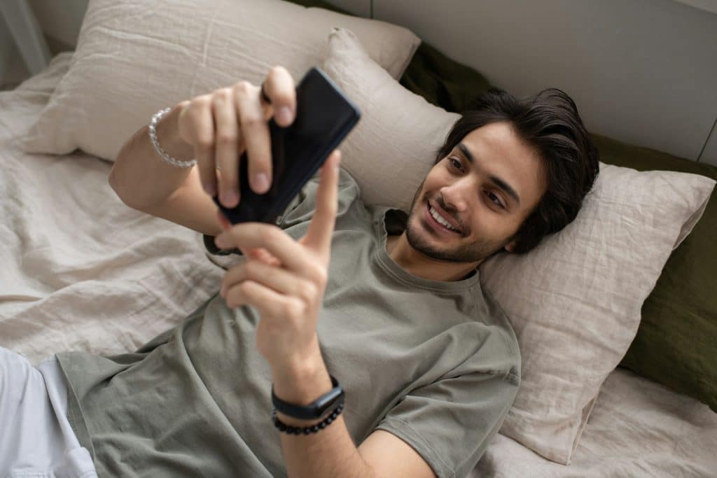 A young man in a gray shirt smiling while texting.