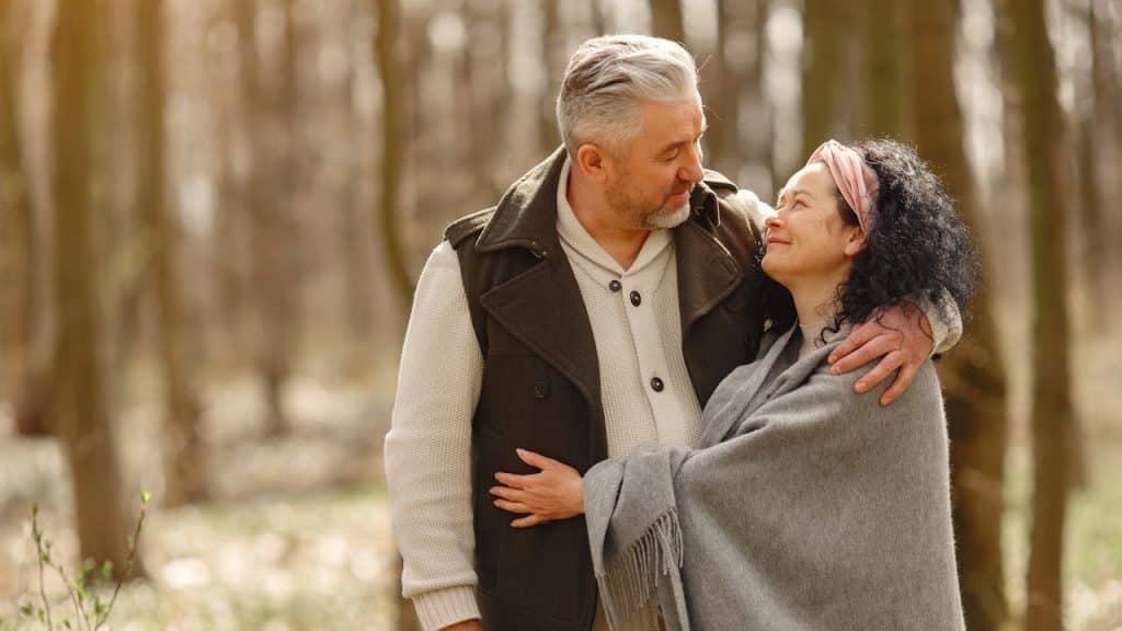 Middle-aged couple embracing and smiling at each other in a wooded area.