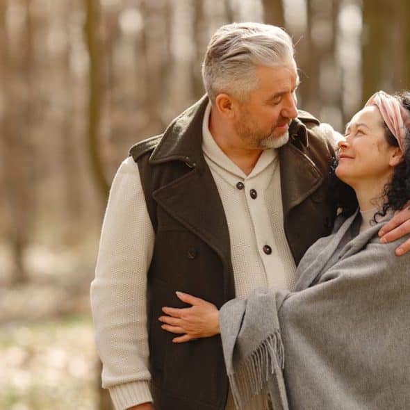 Middle-aged couple embracing and smiling at each other in a wooded area.