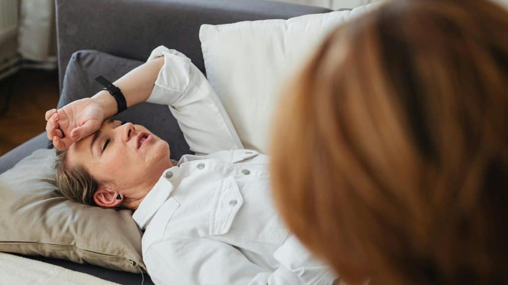 A woman lying on a couch with her hand on her forehead during a therapy session.
